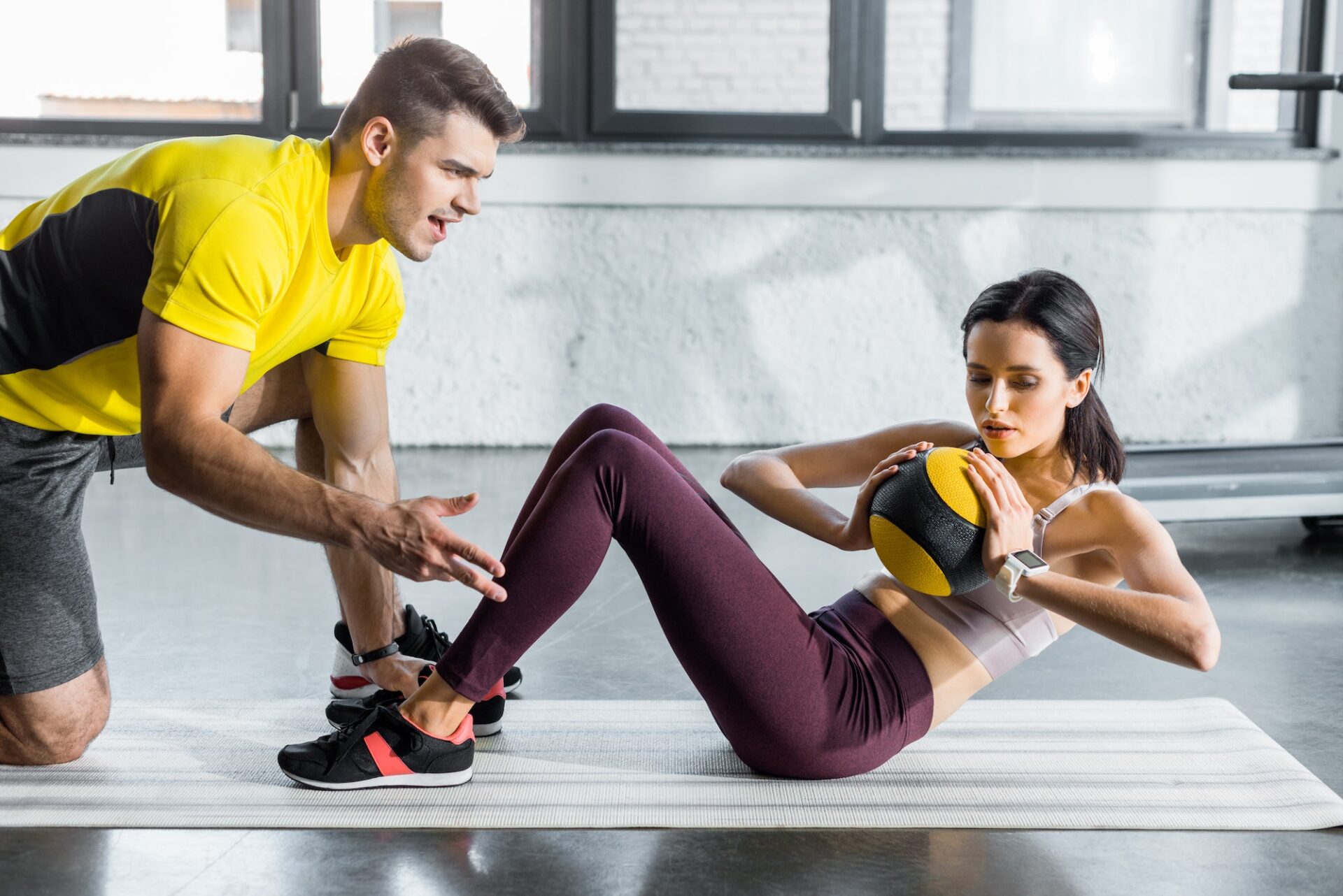 sportswoman doing crunches with ball and sportsman helping her in sports center